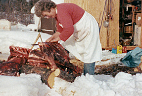 woman butchering a caribou outdoors on a log